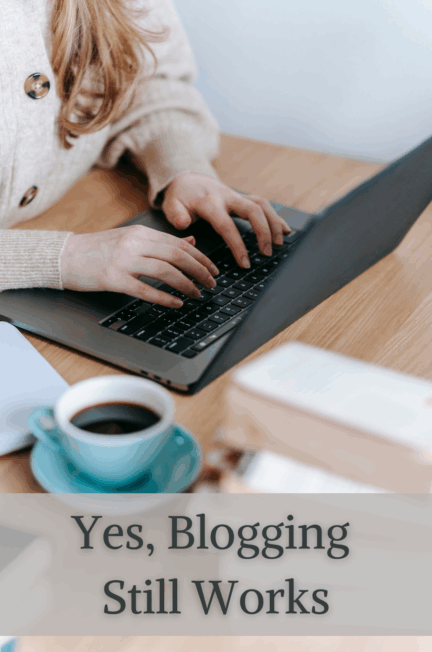 woman typing on a laptop cup of coffee and books on her desk yes, blogging still works